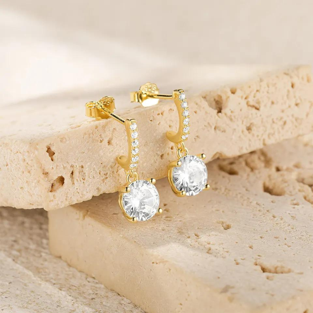 Featuring several small zircons gracefully cascading down to a stunning large zircon at the end of the drop, these earrings radiate a captivating sparkle that adds a touch of glamour to any occasion.